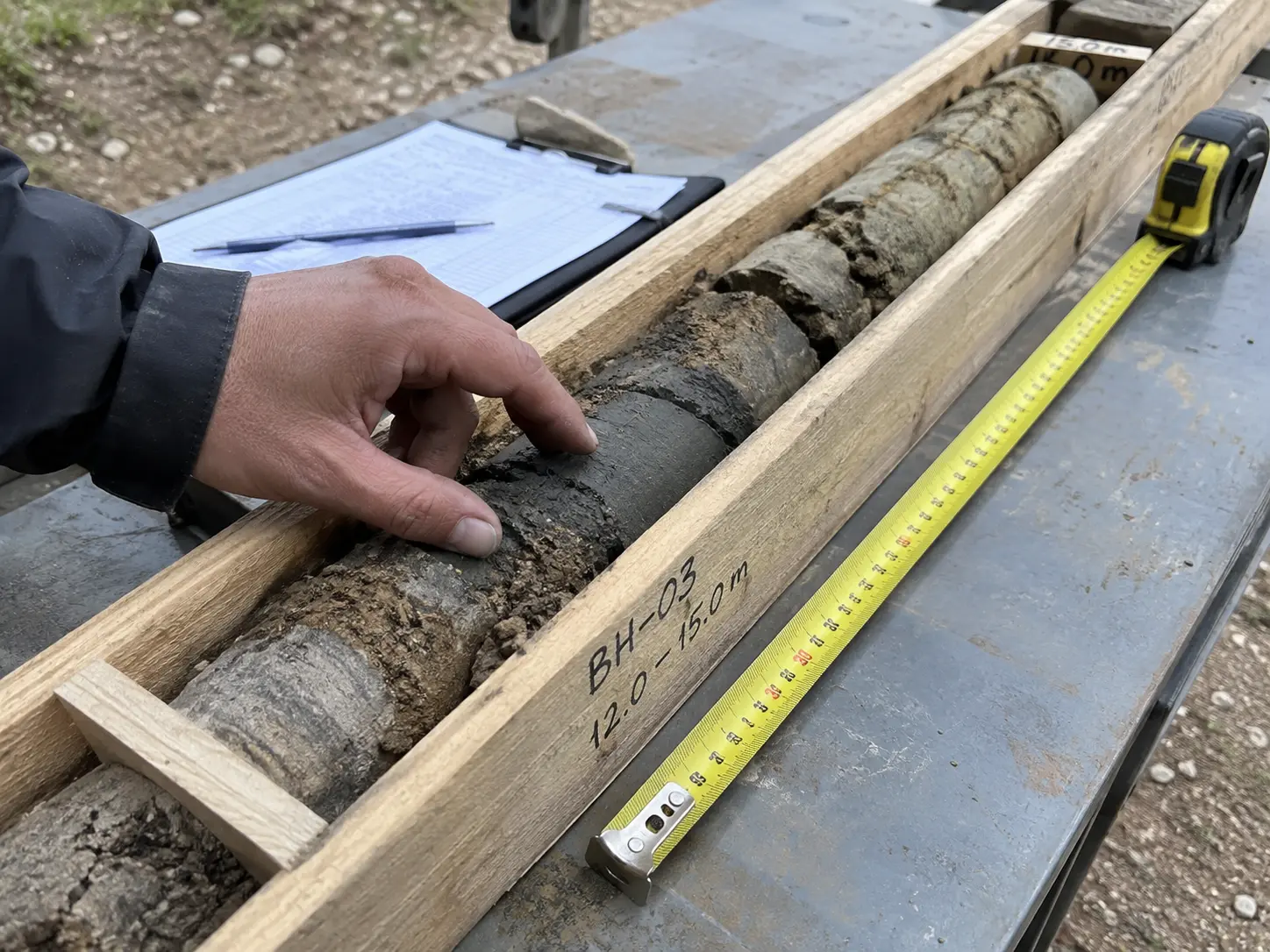 A hand examining a soil sample core in a box for a geotechnical or foundation engineering study