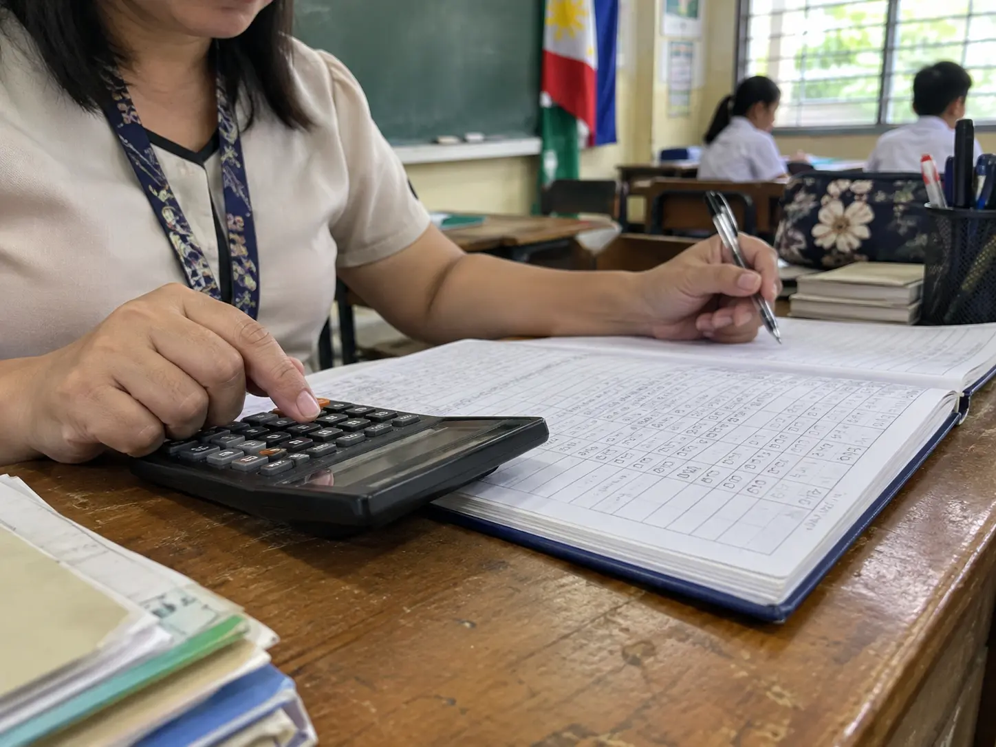 A teacher computing grades in a class record with a calculator